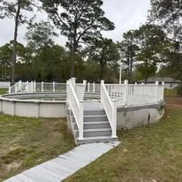 Elevated white composite deck with railing, concrete foundation pad, and wheelchair-accessible ramp on graded yard