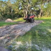 Excavator on residential driveway site with cleared soil and compacted base preparation