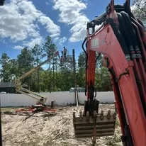 Red excavator with bucket moving soil and debris on cleared construction site