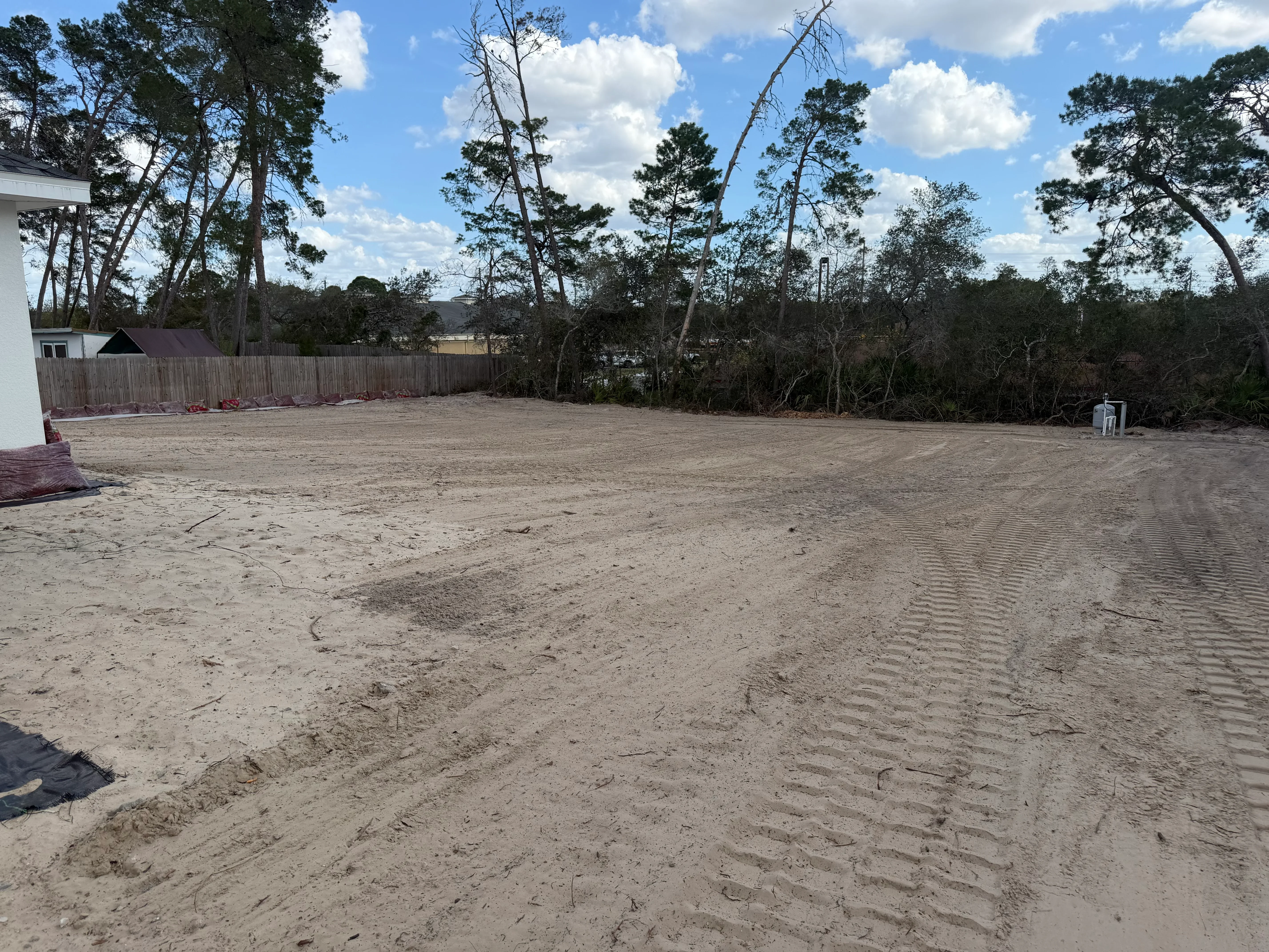 Graded residential lot with compacted soil, wooden perimeter fence, and mature trees
