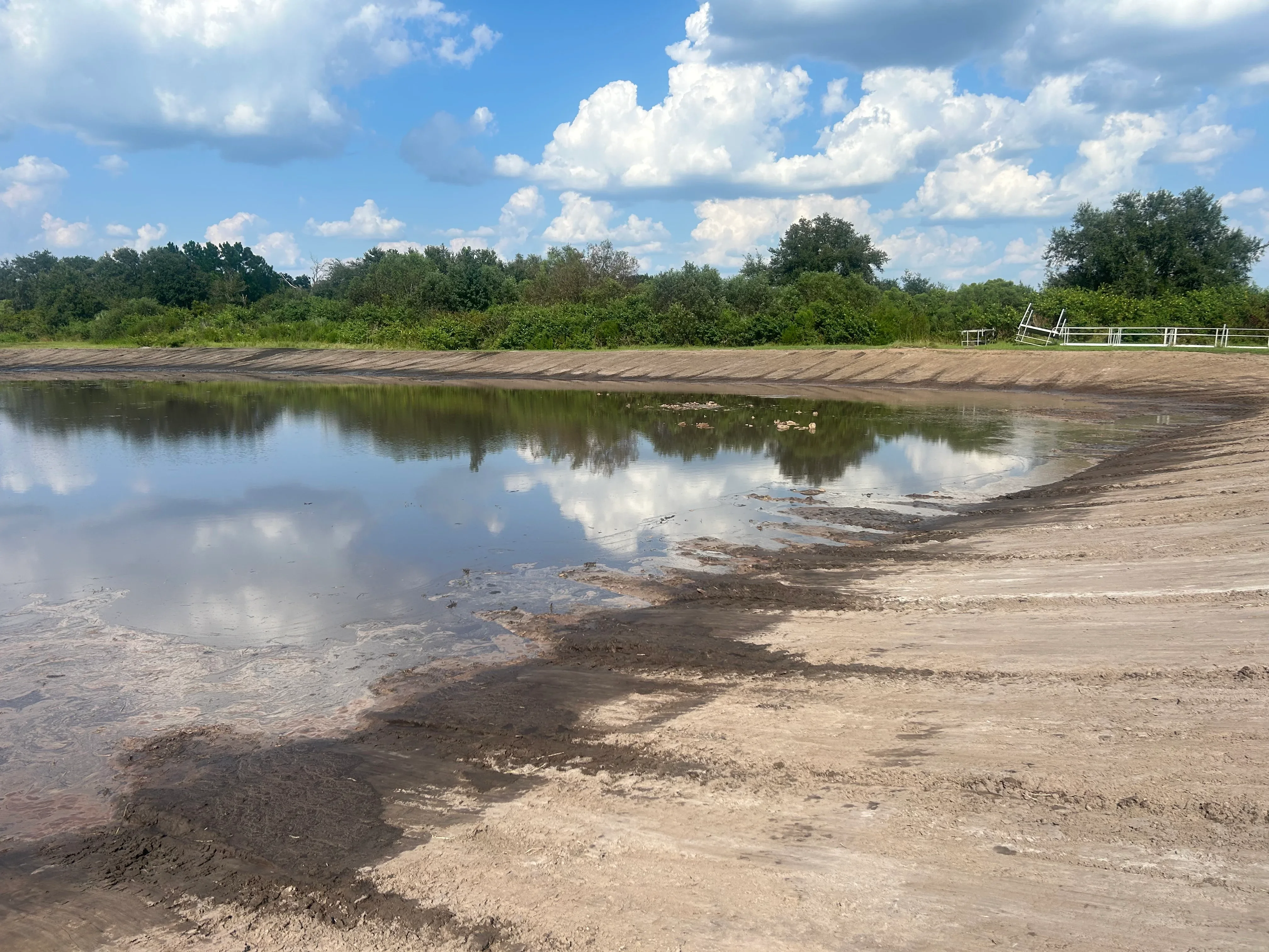 Excavated pond with sloped dirt banks, compacted soil berm, and standing water on rural property