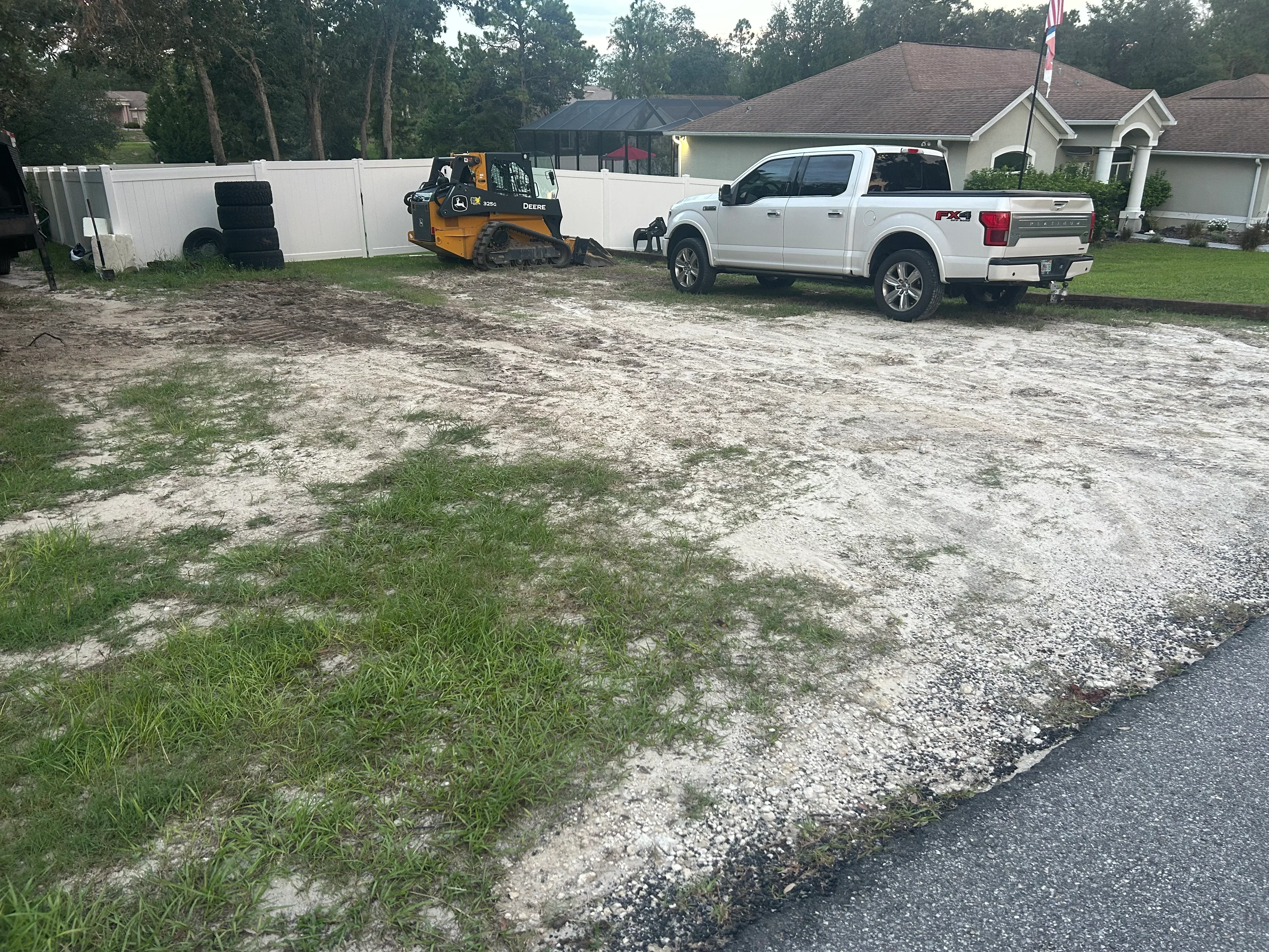 Skid steer loader grading residential lot with gravel base and temporary fencing