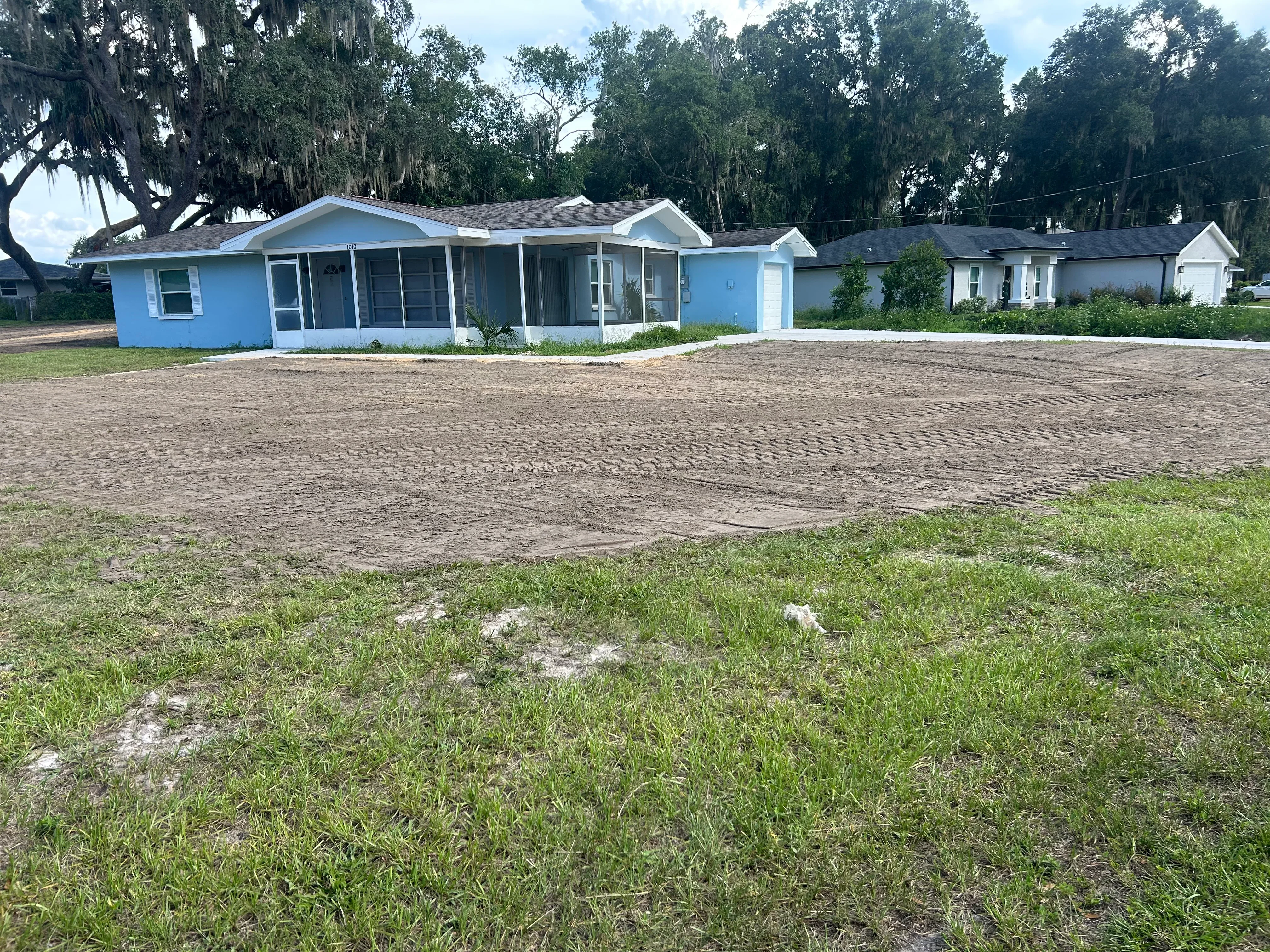 Freshly excavated and graded residential driveway with compacted soil base in front of blue single-story home