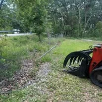 Cleared land with excavation equipment, removed vegetation and debris visible on prepared ground