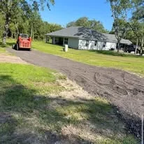 Freshly graded and asphalted driveway with red excavator and residential home in background