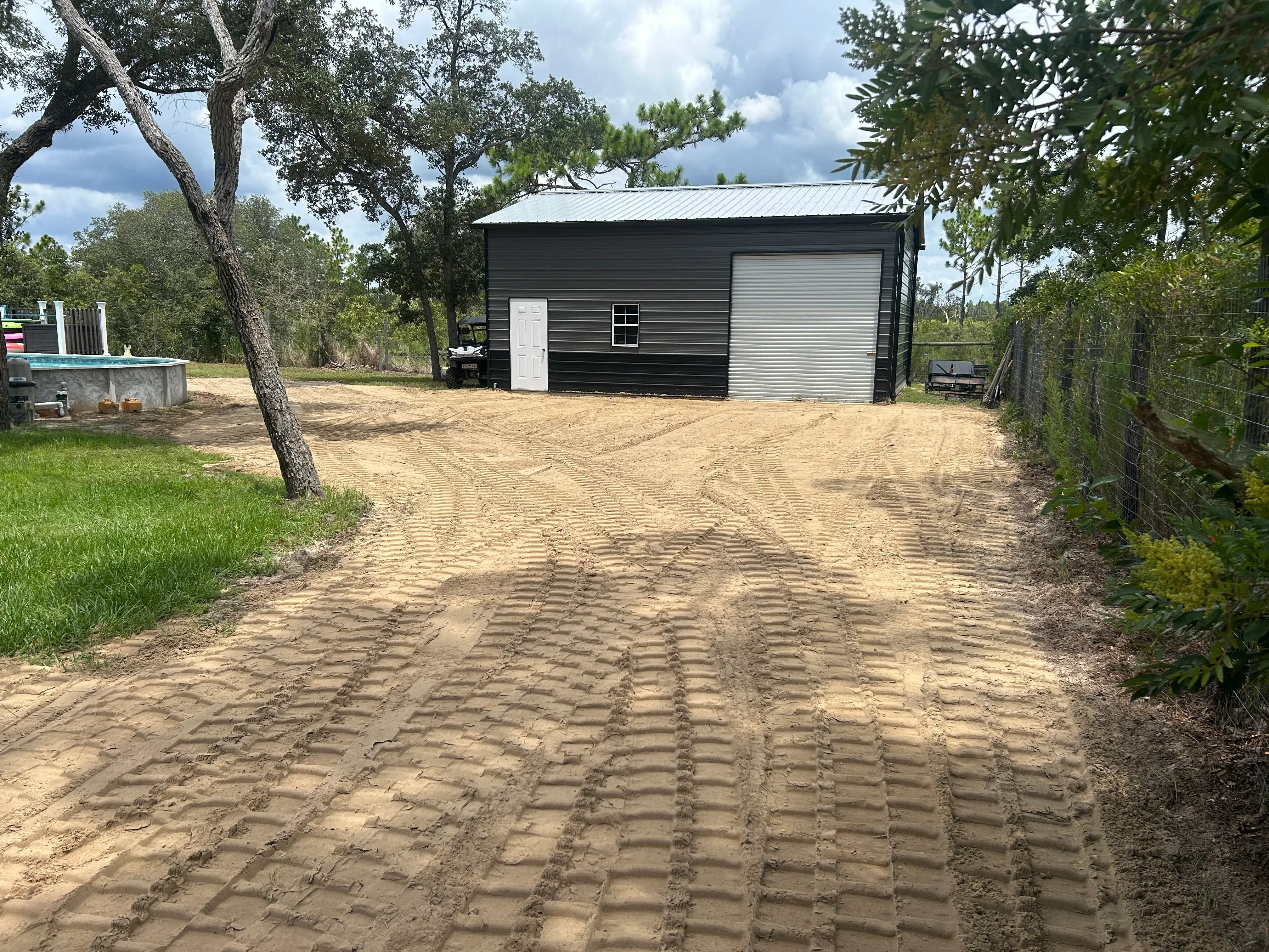 Freshly graded dirt driveway with compacted base and tire tracks leading to black metal building with metal roof
